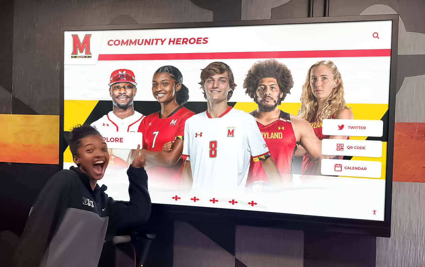 Student pointing at Community Heroes digital display showcasing athletes