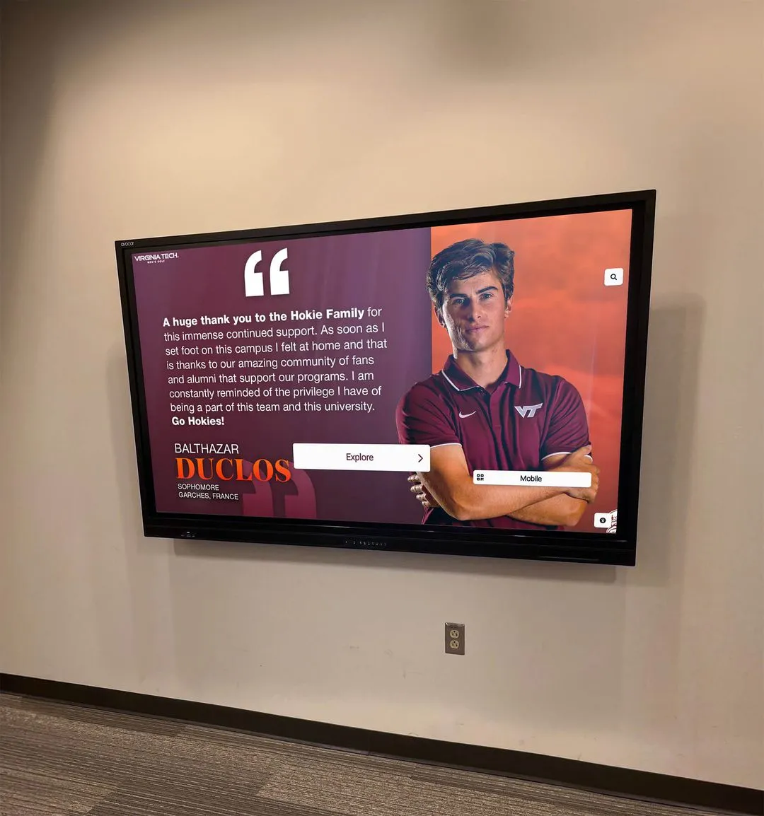 Virginia Tech student-athlete standing by wall display in maroon polo